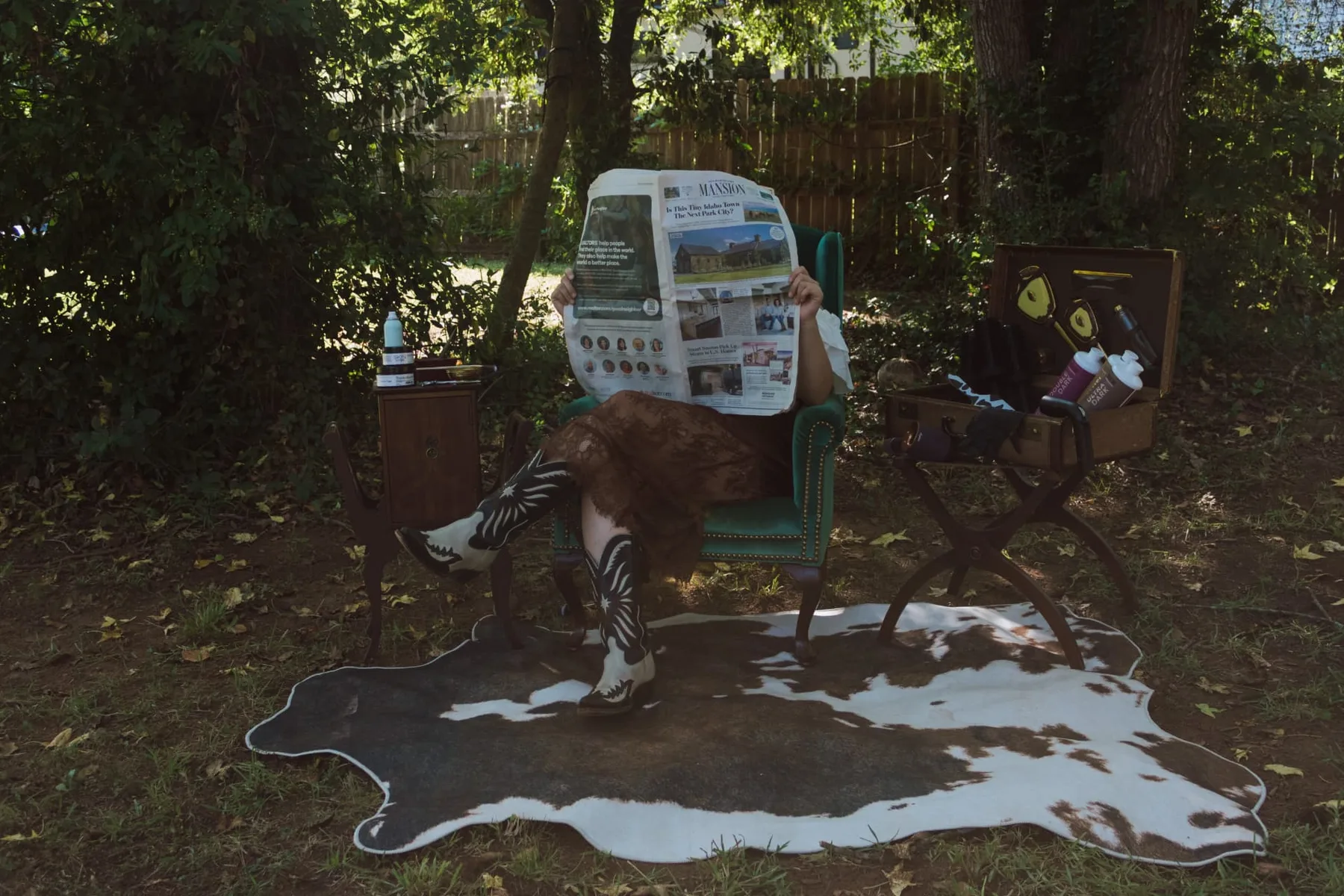Outdoor salon set up under the trees: green velvet chair, cowhide rug and western boots