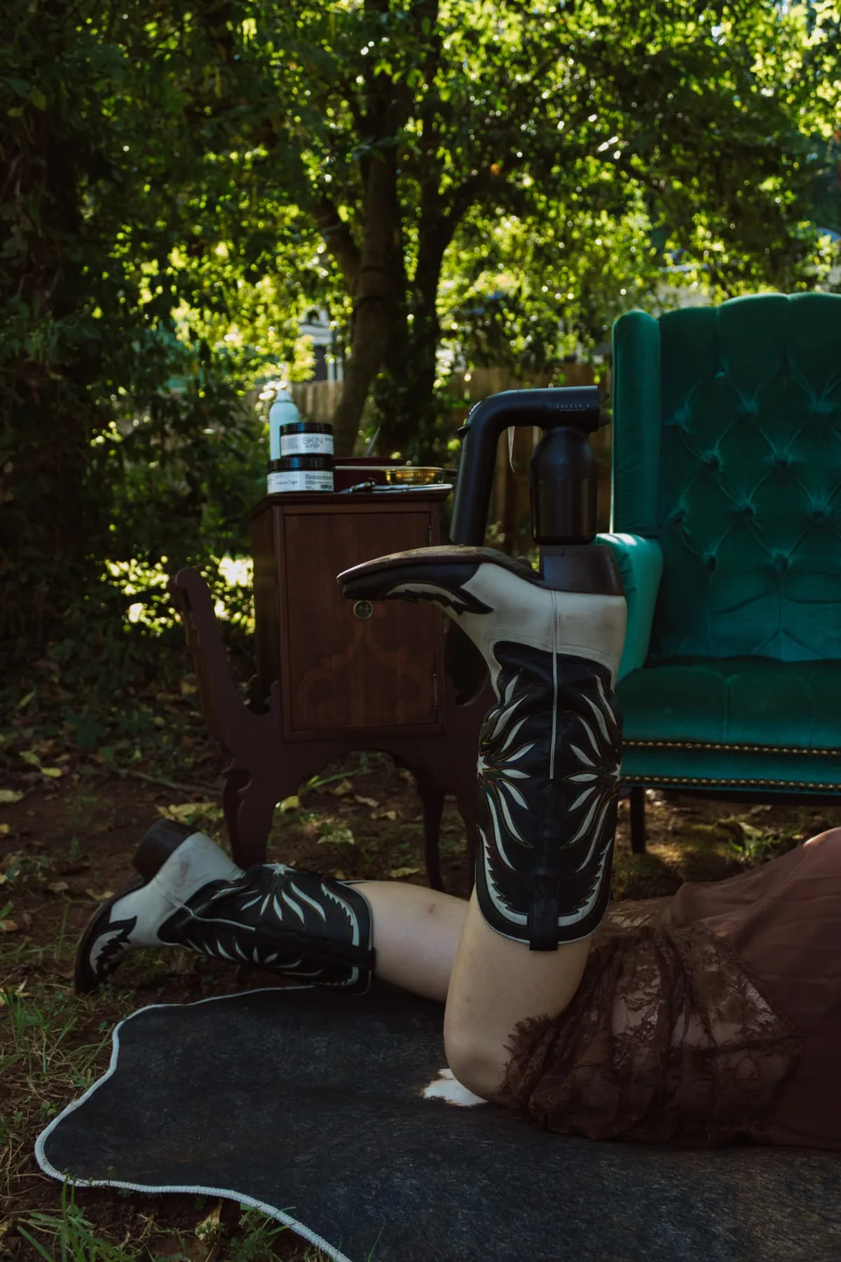 Embroidered western boots resting beside a spray tan wand and vintage side table
